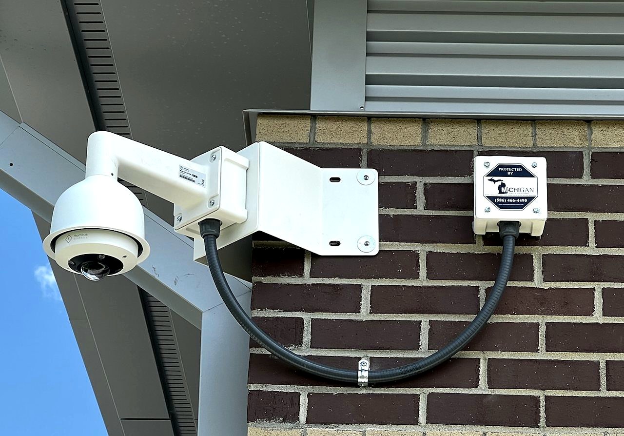 Michigan Security Systems commercial security camera with Protected By sign on brick building exterior
