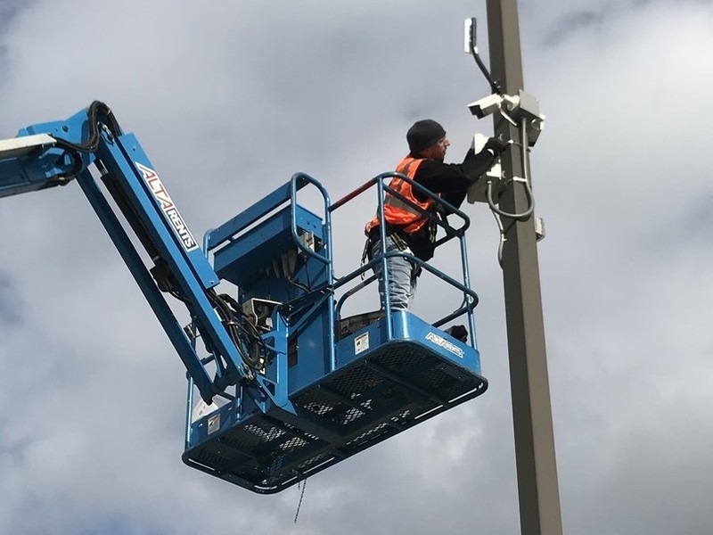 Michigan Security Systems technician mounting commercial Digital Watchdog security cameras on a parking lot light pole from a boom lift