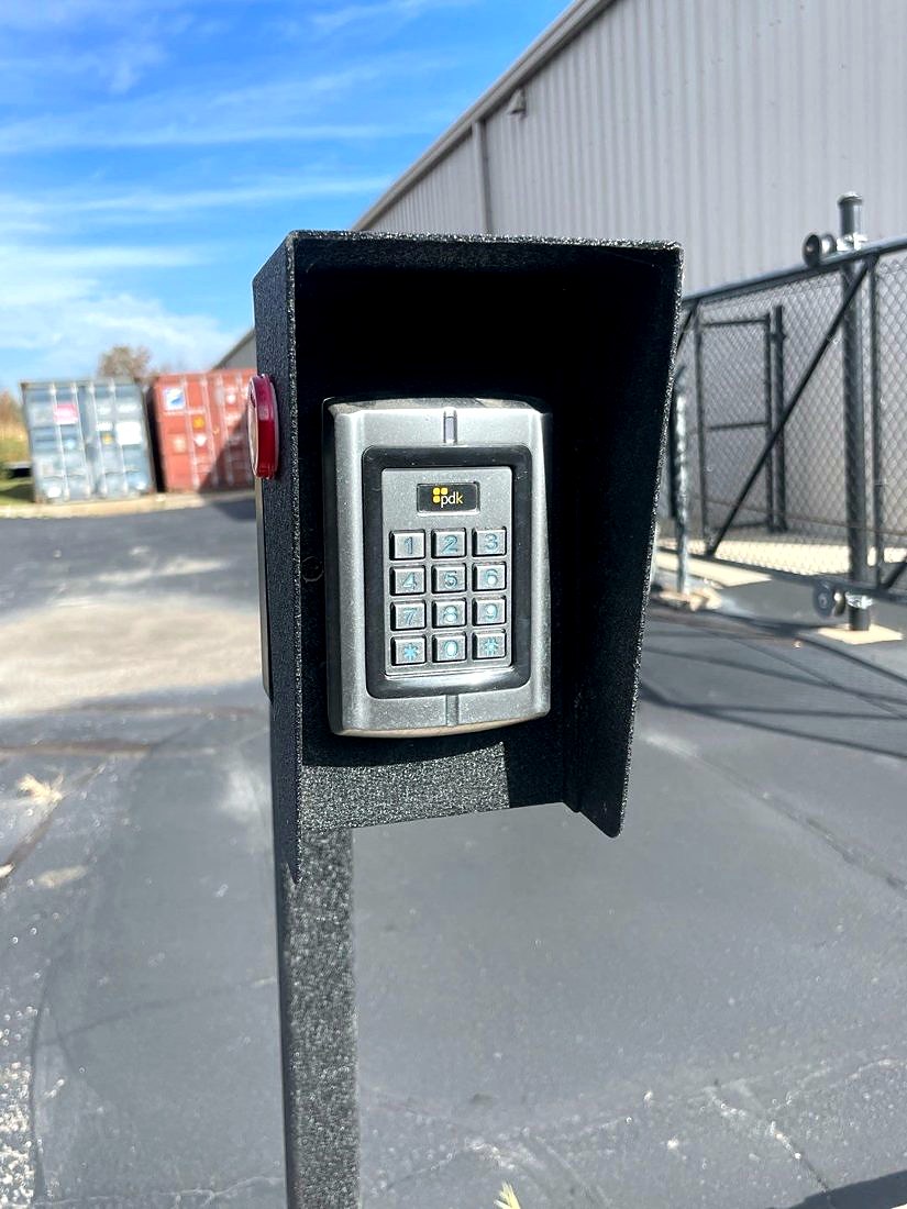 Pedestal-mounted PDK access control keypad reader in a weather hood at the yard gate entrance at Merlo Construction in Milford, Michigan, installed by Michigan Security Systems