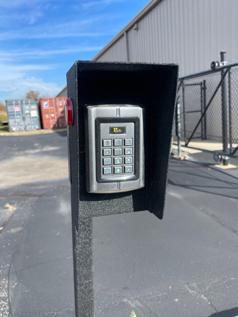 Pedestal-mounted PDK access control keypad reader in a weather hood at the yard gate entrance at Merlo Construction in Milford, Michigan, installed by Michigan Security Systems