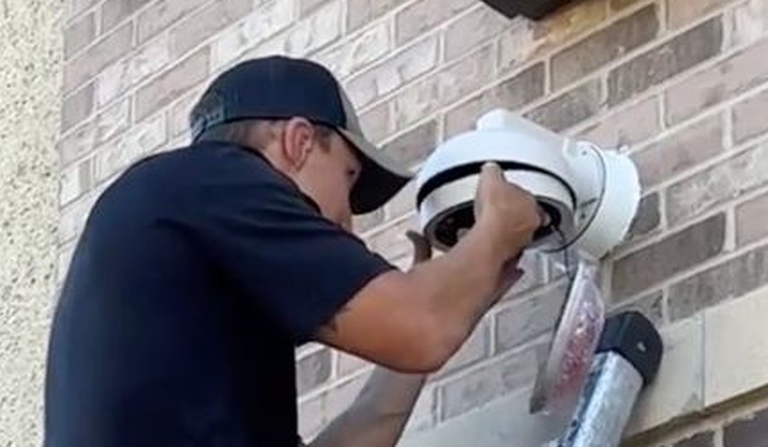 Michigan Security Systems technician on ladder installing a dome security camera on brick wall at Shelby Township Water Department, Macomb County MI