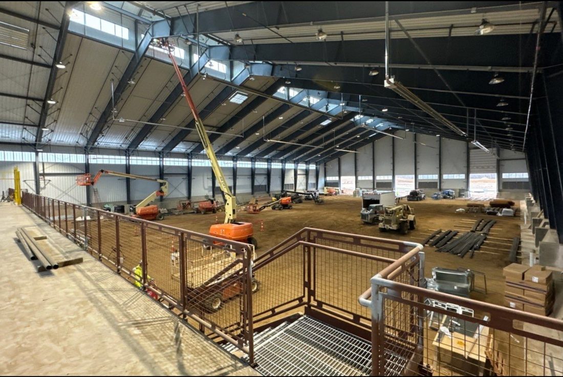 Interior of the IUOE Local 324 training arena in Howell, Michigan during construction, with boom lifts running cabling through the steel structure for the Michigan Security Systems camera and access control installation