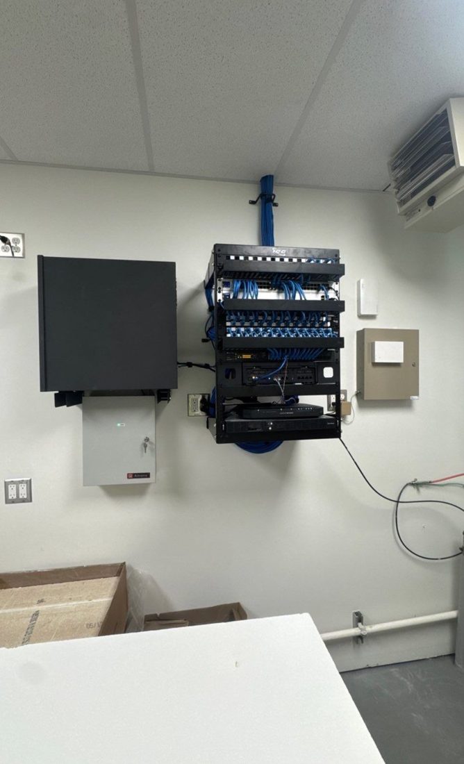 Wall-mounted network rack with ICC patch panels, blue structured cabling, network switches, an NVR recorder, and an Altronix power supply at The Learning Experience childcare center in Michigan, installed by Michigan Security Systems