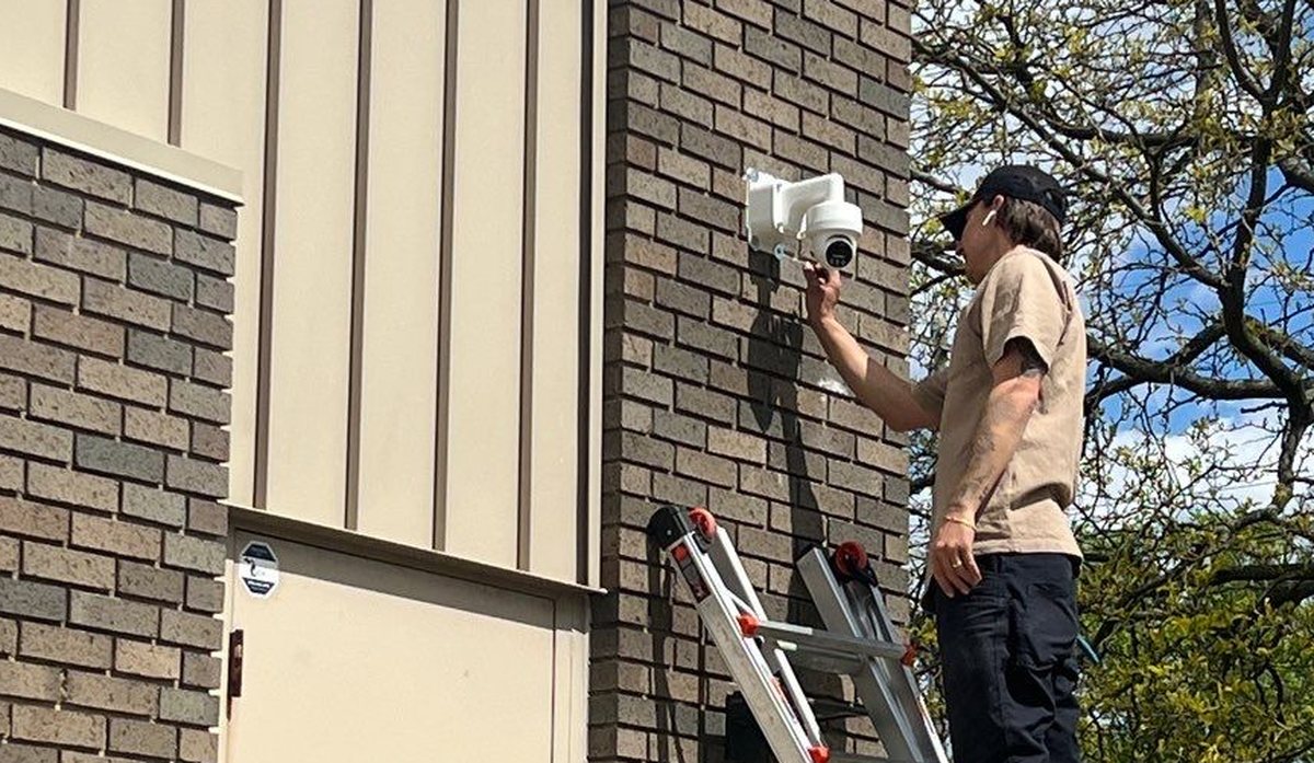 Michigan Security Systems technician installing a security camera on a ladder at a New Baltimore municipal building