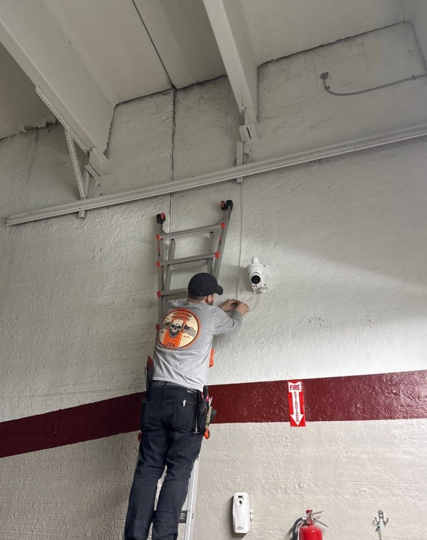 Michigan Security Systems technician on a ladder installing a wall-mounted security camera during the camera and alarm upgrade at the Chesterfield Library in Chesterfield, Michigan