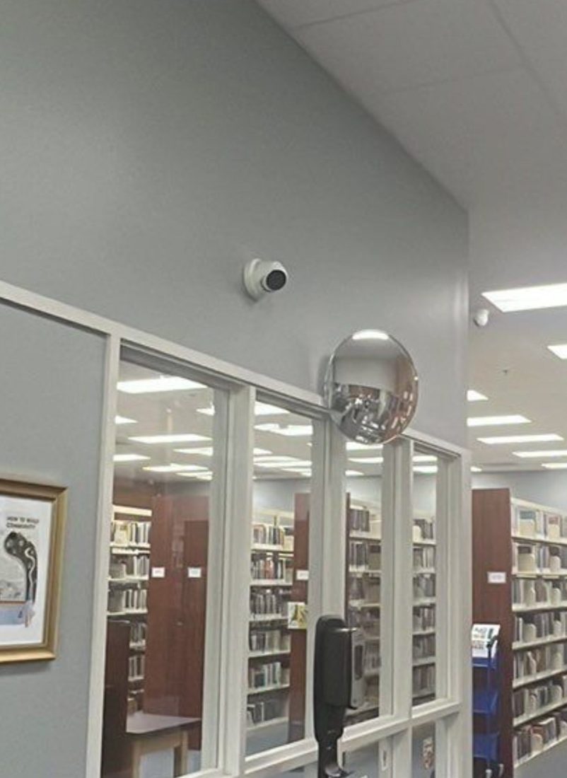 Wide-angle 8MP security camera mounted high on the wall covering the book stacks and reading area at the Chesterfield Library in Chesterfield, Michigan, installed by Michigan Security Systems