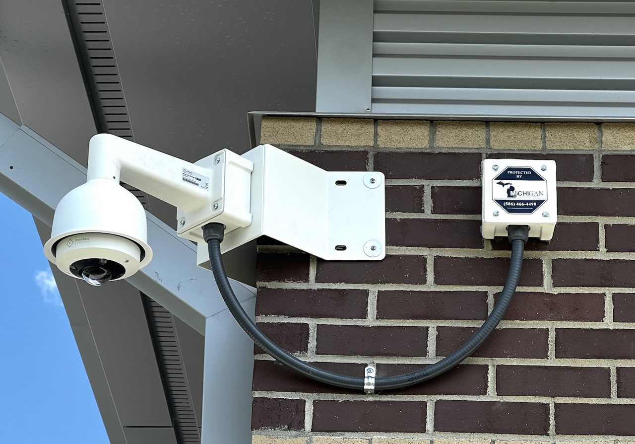 Michigan Security Systems commercial security camera with Protected By sign on brick building exterior