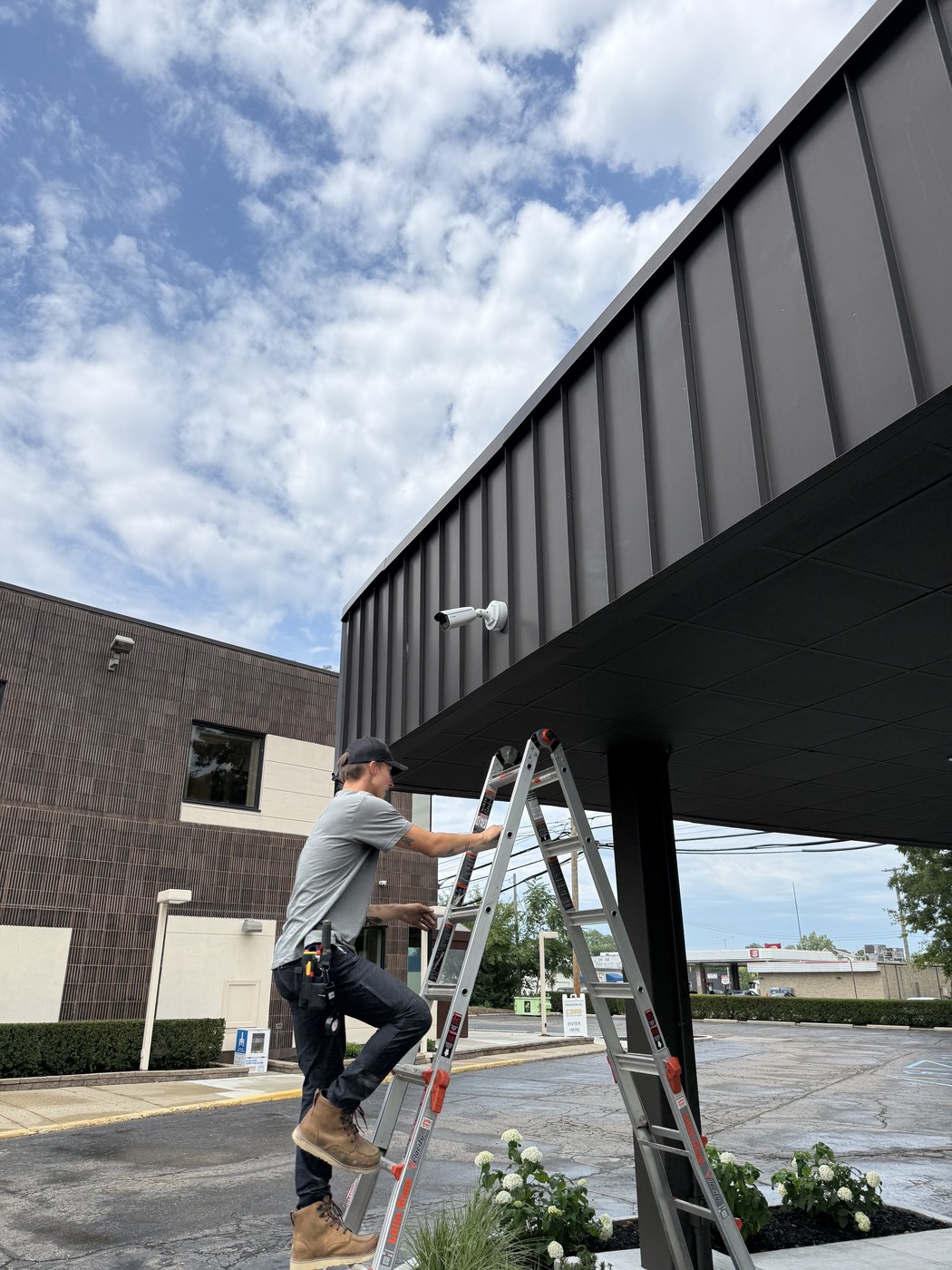Michigan Security Systems technician installing a security camera under a healthcare facility entrance canopy