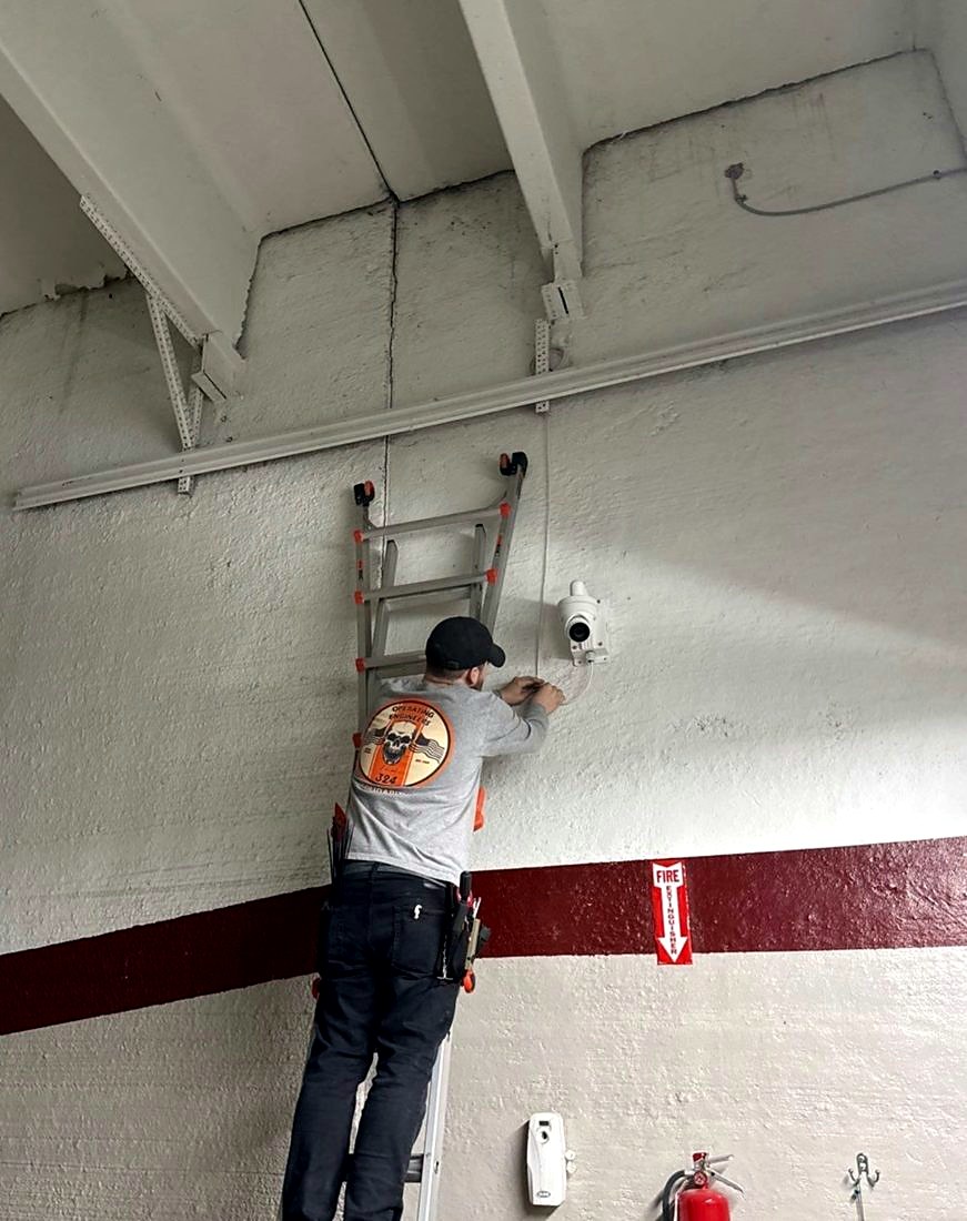 Michigan Security Systems technician on a ladder installing a wall-mounted security camera during the camera and alarm upgrade at the Chesterfield Library in Chesterfield, Michigan