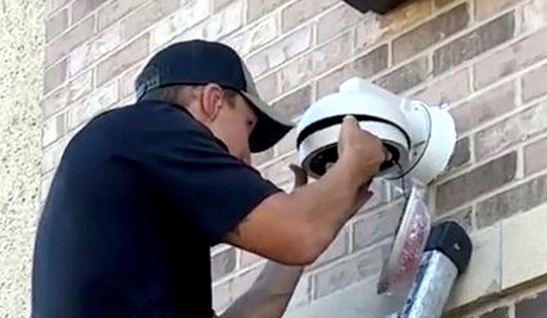 Michigan Security Systems technician on ladder installing a dome security camera on brick wall at Shelby Township Water Department, Macomb County MI