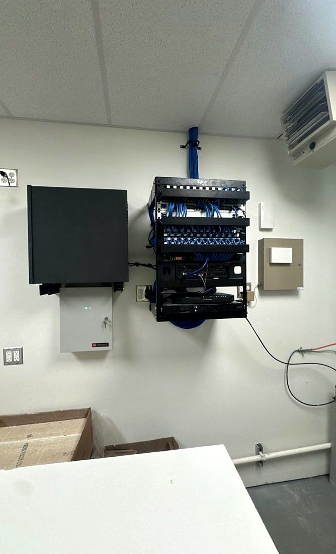Wall-mounted network rack with ICC patch panels, blue structured cabling, network switches, an NVR recorder, and an Altronix power supply at The Learning Experience childcare center in Michigan, installed by Michigan Security Systems