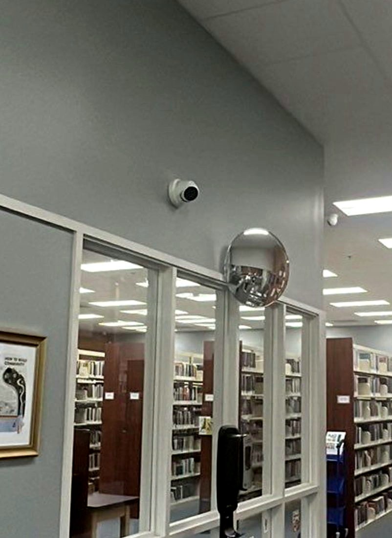 Wide-angle 8MP security camera mounted high on the wall covering the book stacks and reading area at the Chesterfield Library in Chesterfield, Michigan, installed by Michigan Security Systems